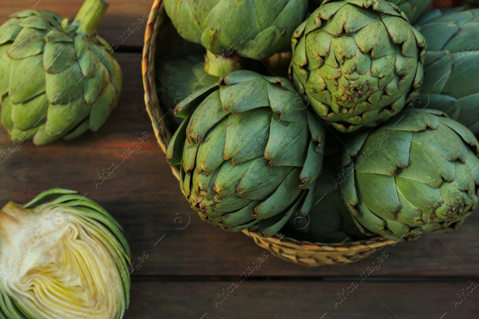 Photo of Whole and cut fresh raw artichokes on wooden table, flat lay