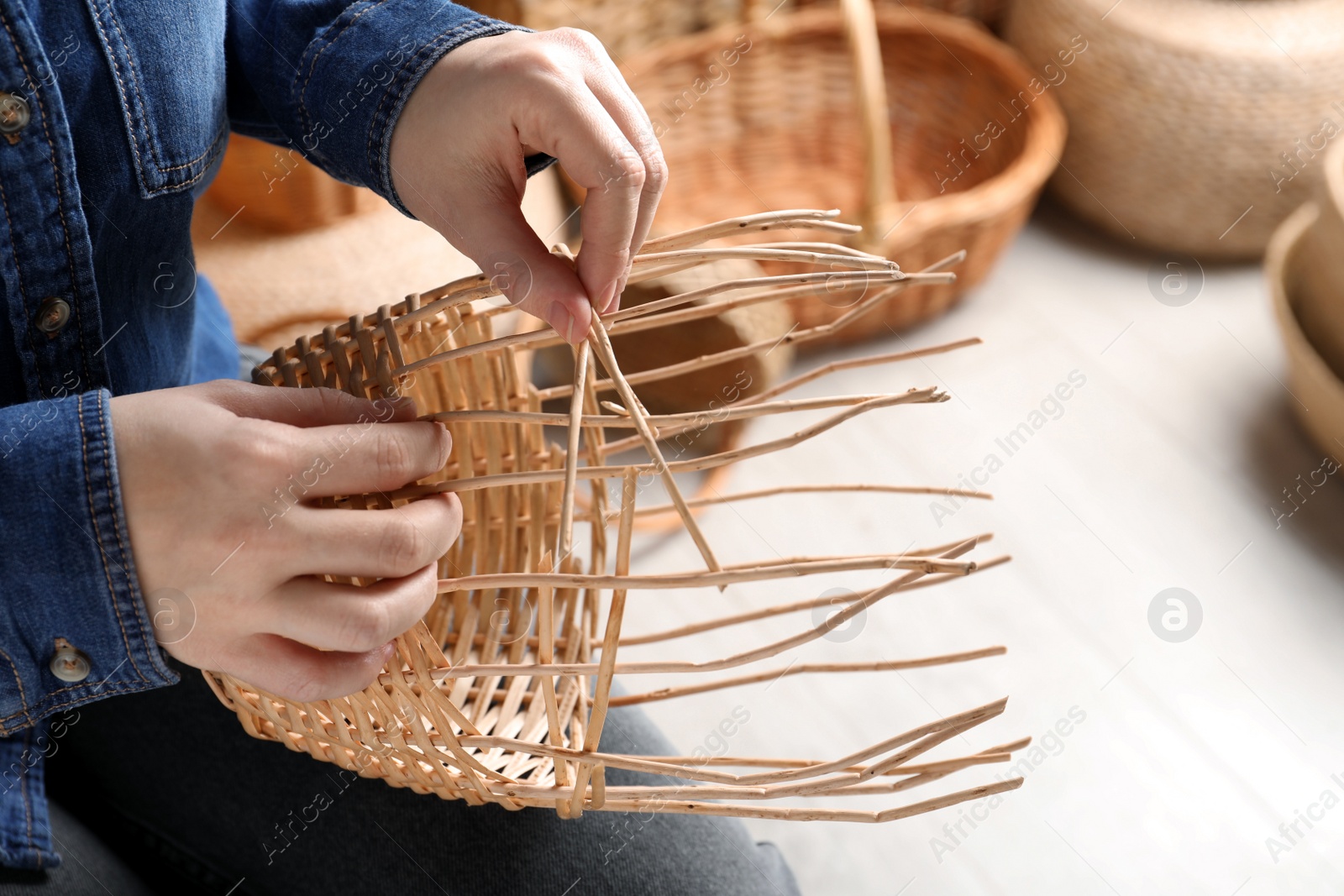 Photo of Woman weaving wicker basket indoors, closeup view