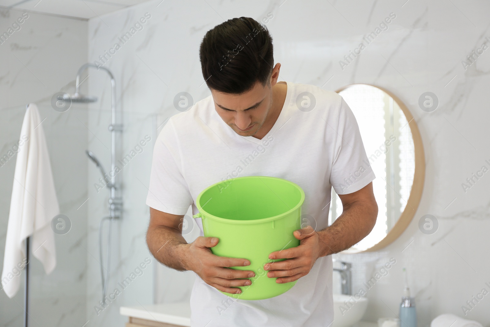 Photo of Man with bucket suffering from nausea in bathroom. Food poisoning