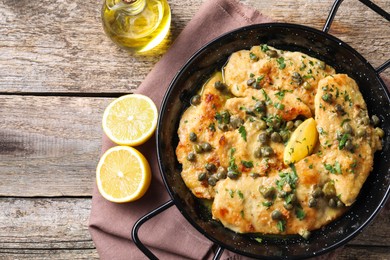 Delicious chicken piccata with herbs and lemon on wooden table, flat lay