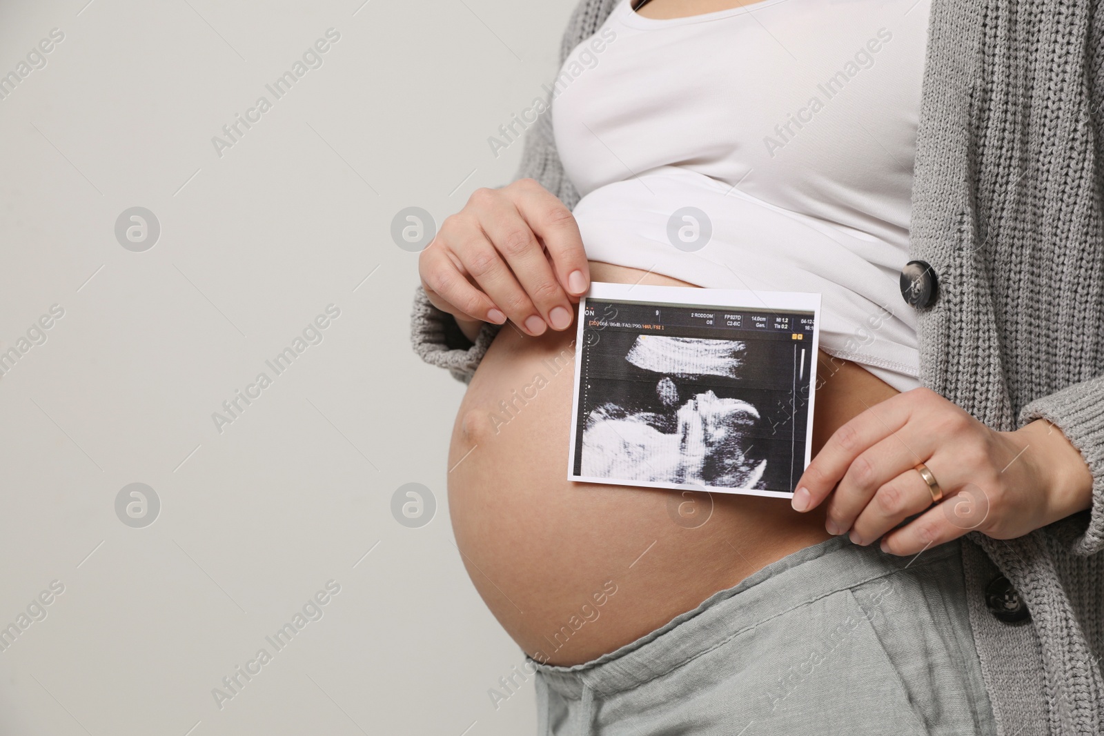 Photo of Young pregnant woman with ultrasound picture of baby on grey background, closeup. Space for text