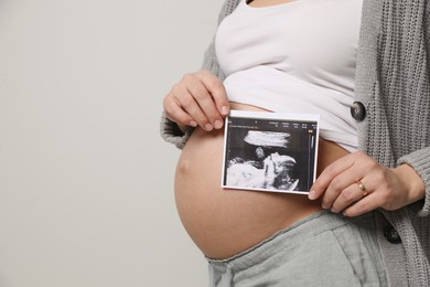 Photo of Young pregnant woman with ultrasound picture of baby on grey background, closeup. Space for text