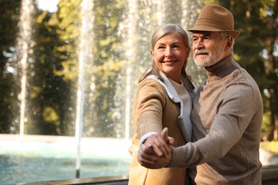 Photo of Affectionate senior couple dancing together near fountain outdoors, space for text