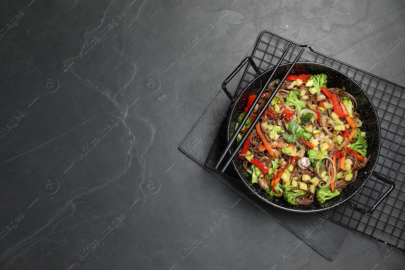 Photo of Stir fried noodles with mushrooms and vegetables in wok on black table, top view. Space for text