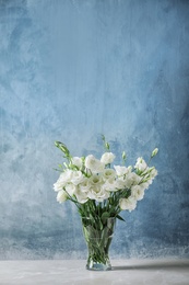 Photo of Vase with beautiful Eustoma flowers on table against color background