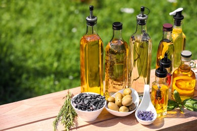 Photo of Different cooking oils and ingredients on wooden table against blurred green background. Space for text