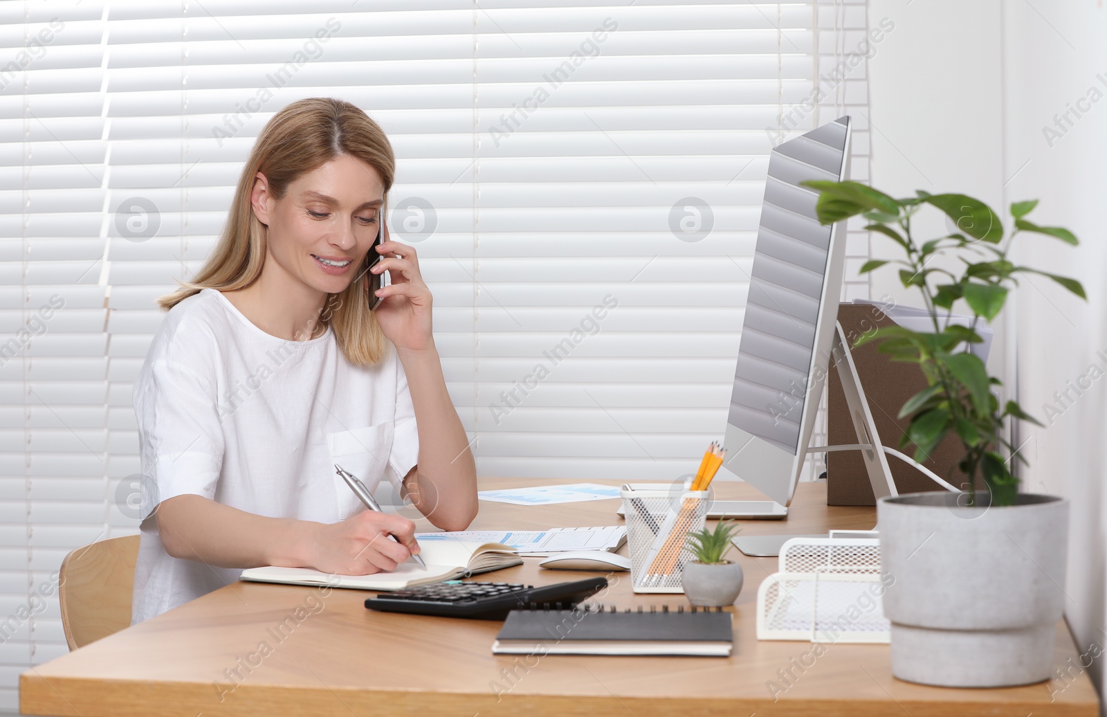 Photo of Professional accountant talking on phone while working at wooden desk in office