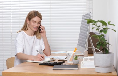 Professional accountant talking on phone while working at wooden desk in office