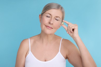 Photo of Beautiful woman with vitamin capsule on light blue background