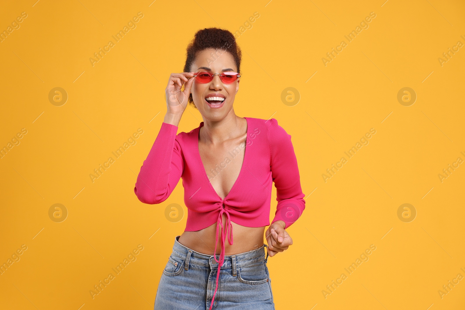 Photo of Happy young woman in stylish sunglasses dancing on orange background