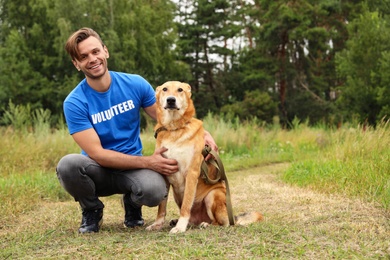Photo of Male volunteer with homeless dog at animal shelter outdoors