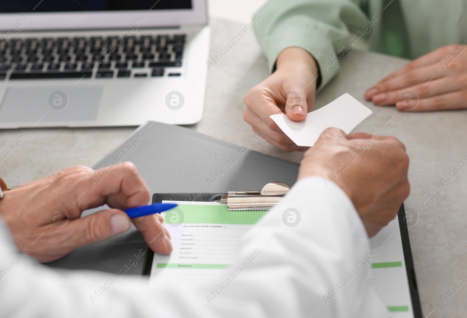 Photo of Doctor giving prescription to patient while filling medical card at table in clinic, closeup