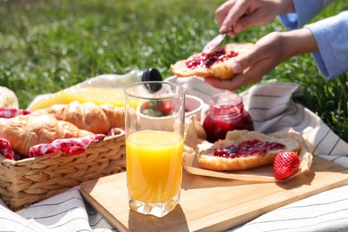 Photo of Woman with croissant outdoors, focus on glass of juice. Summer picnic
