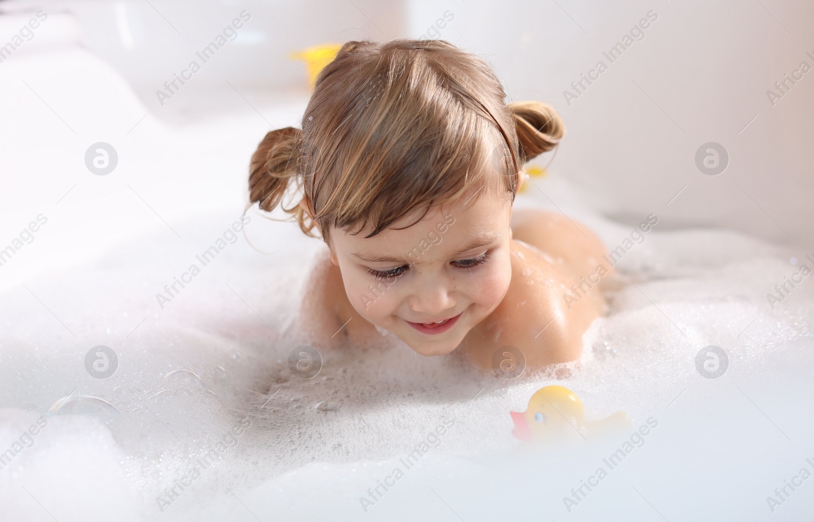 Photo of Smiling girl bathing with toy duck in tub