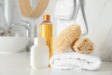 Natural loofah sponges, towel and cosmetic products on table in bathroom