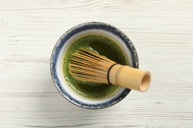 Cup of fresh matcha tea with bamboo whisk on white wooden table, top view