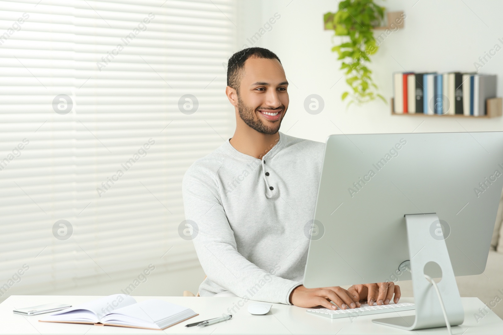 Photo of Young man working on computer at desk in room. Home office