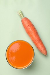 Glass with healthy carrot juice on light green background, top view