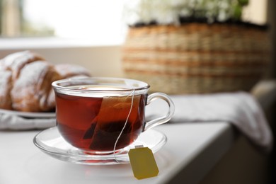 Photo of Tea bag in glass cup on white windowsill, closeup. Space for text