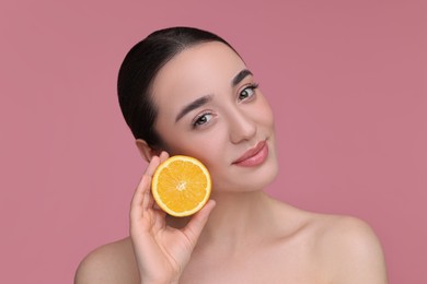 Beautiful young woman with piece of orange on pink background