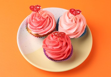 Photo of Delicious cupcakes with bright cream and heart toppers on orange background