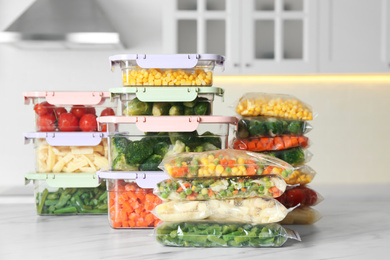 Photo of Plastic bags and containers with different frozen vegetables on white marble table in kitchen