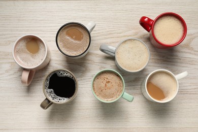 Many cups with different aromatic coffee on light wooden table, flat lay