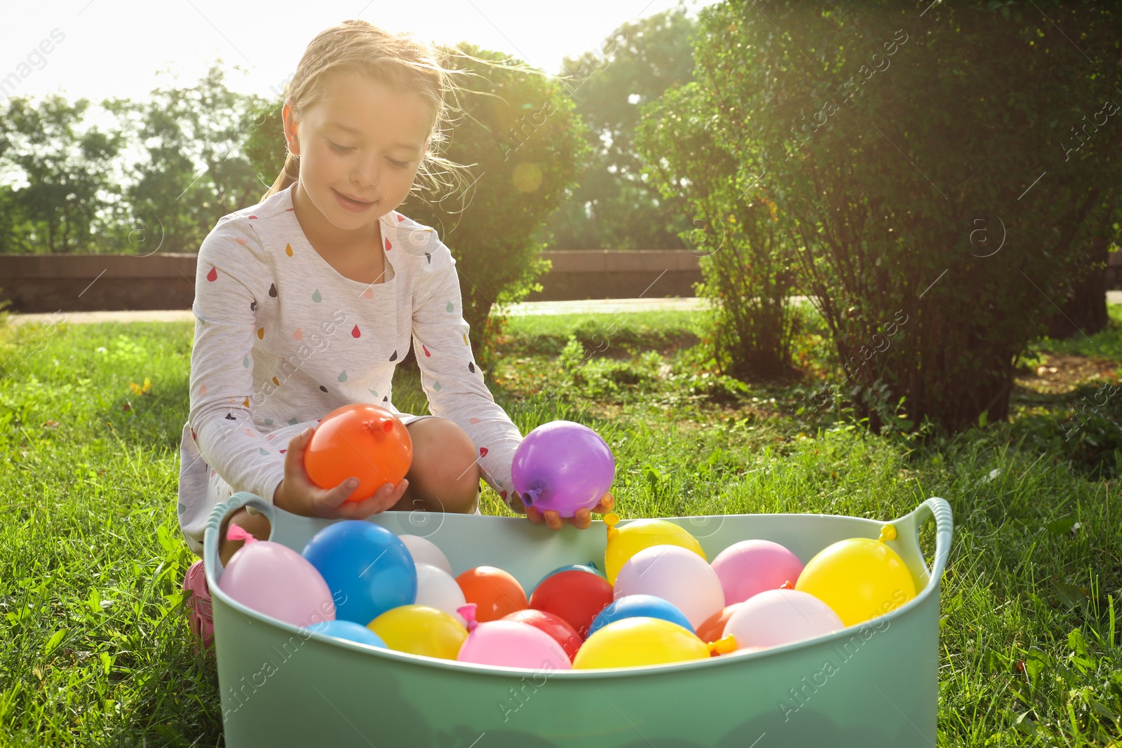 Photo of Little girl with basin of water bombs in park on sunny day