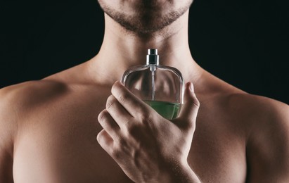 Image of Handsome man with bottle of perfume on black background, closeup