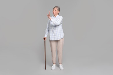 Photo of Senior woman with walking cane waving on gray background
