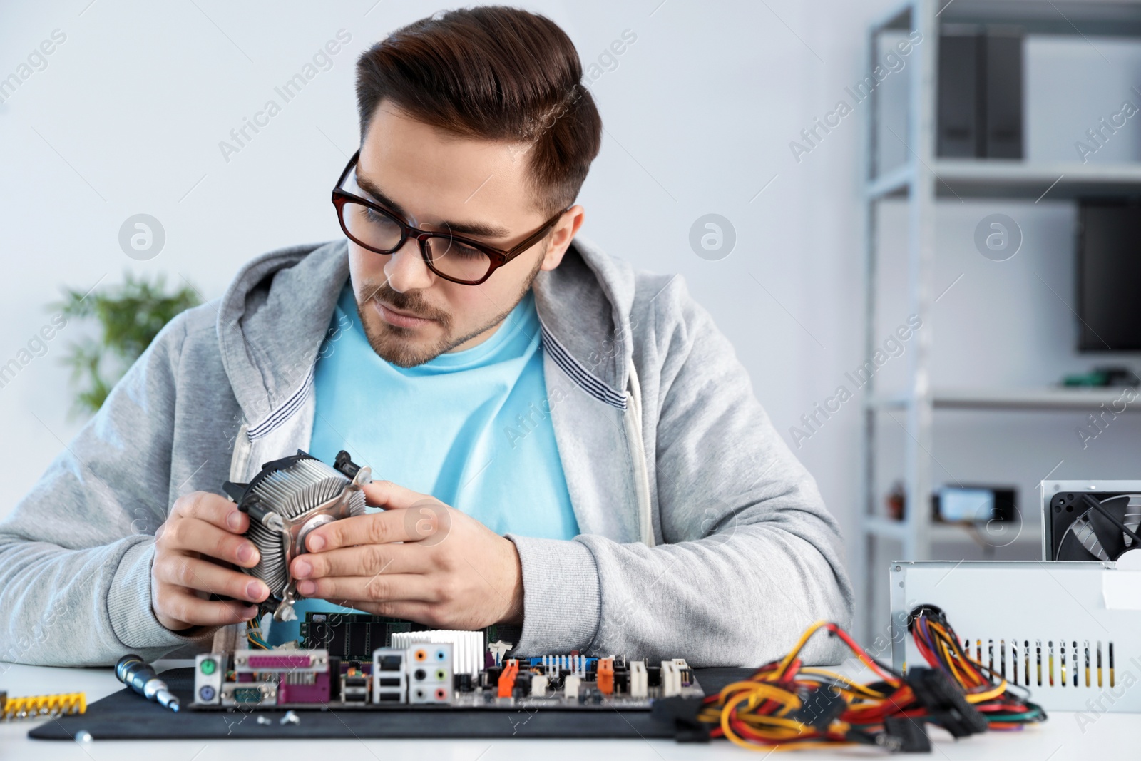 Photo of Male technician repairing motherboard at table indoors