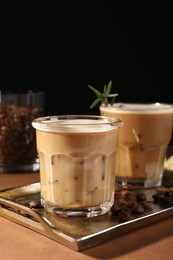 Photo of Refreshing iced coffee with milk in glasses and beans on brown table against black background, space for text