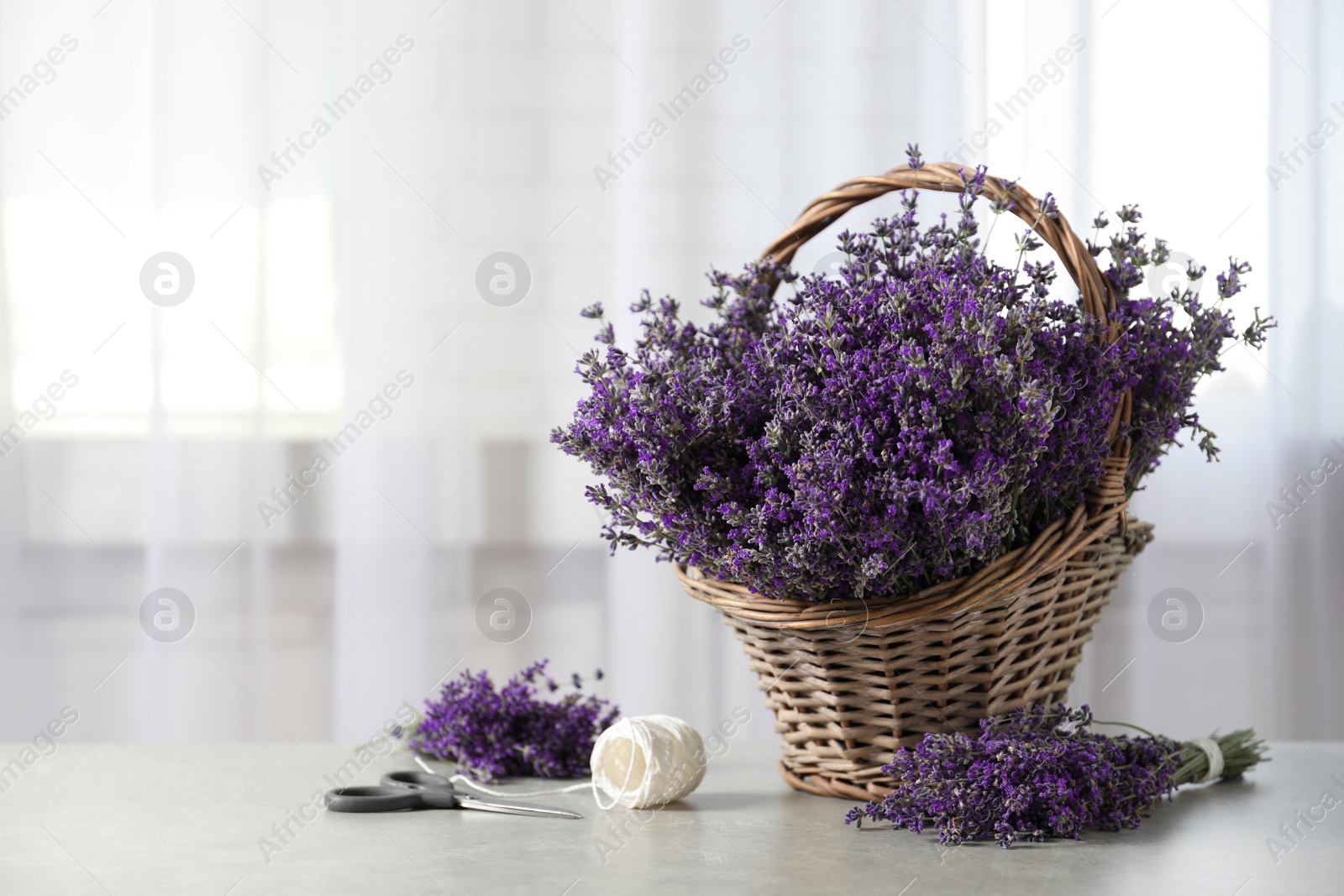 Photo of Fresh lavender flowers in basket on stone table indoors, space for text