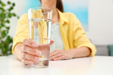 Woman holding glass of water at white table, closeup with space for text. Refreshing drink