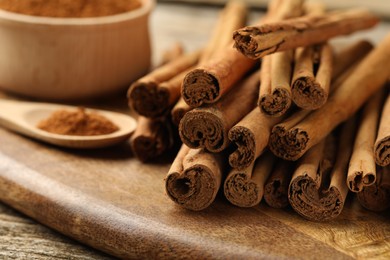 Photo of Cinnamon powder and sticks on wooden table, closeup