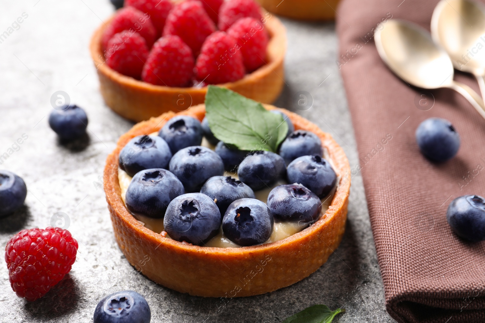 Photo of Tartlet with fresh blueberries on light grey table, closeup. Delicious dessert