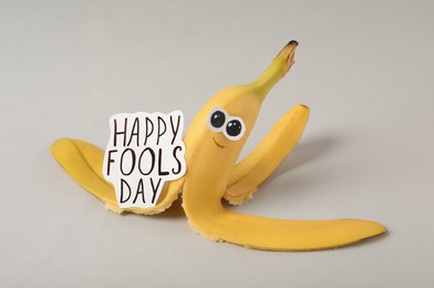 Photo of Banana peel with words Happy Fool's Day on light grey background