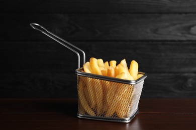 Photo of Frying basket with tasty french fries on wooden table