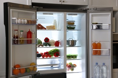 Photo of Open refrigerator full of different products in kitchen