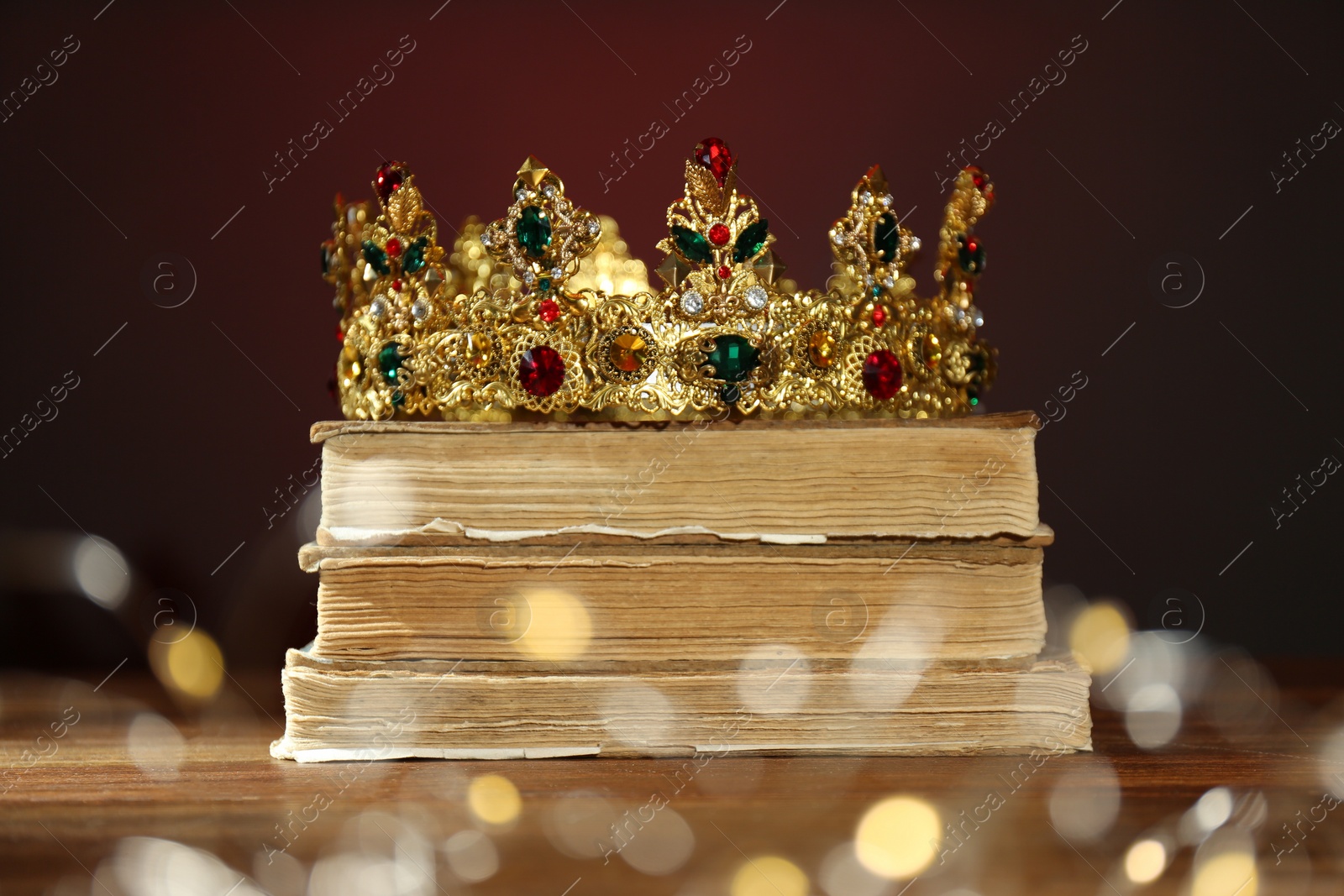 Photo of Beautiful golden crown, old books and fairy lights on brown background. Fantasy item