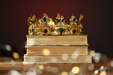 Photo of Beautiful golden crown, old books and fairy lights on brown background. Fantasy item