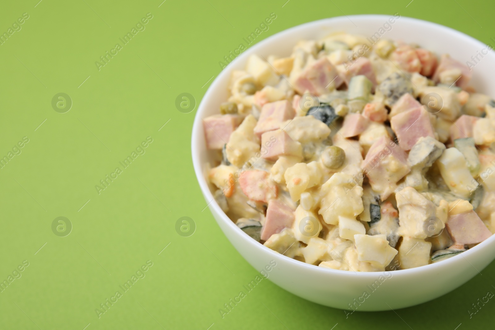 Photo of Tasty Olivier salad with boiled sausage in bowl on green table. Space for text