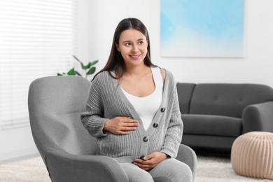 Photo of Beautiful pregnant woman sitting in armchair at home