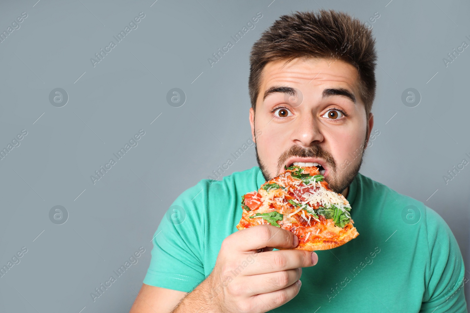 Photo of Handsome man eating pizza on grey background, space for text