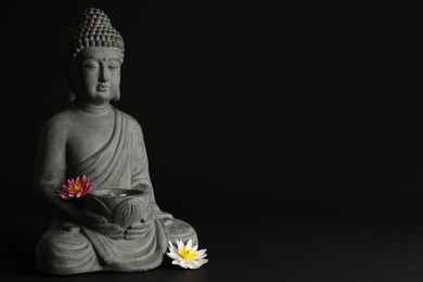 Photo of Beautiful stone Buddha sculpture with flowers on black background. Space for text