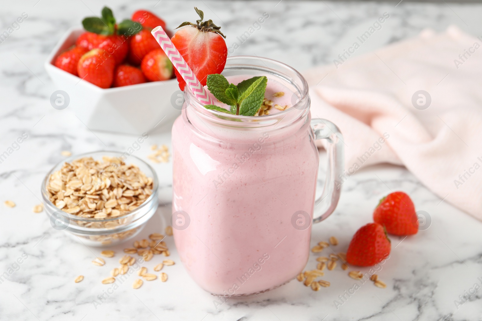 Photo of Mason jar of tasty strawberry smoothie with oatmeal and mint on white marble table