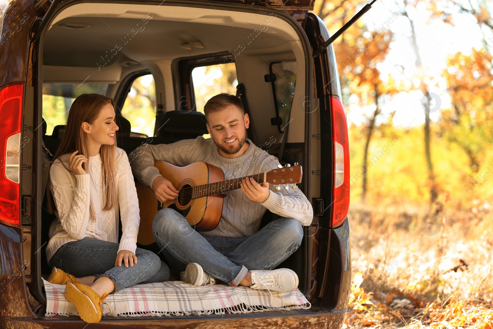 Photo of Young couple with guitar sitting in open car trunk outdoors