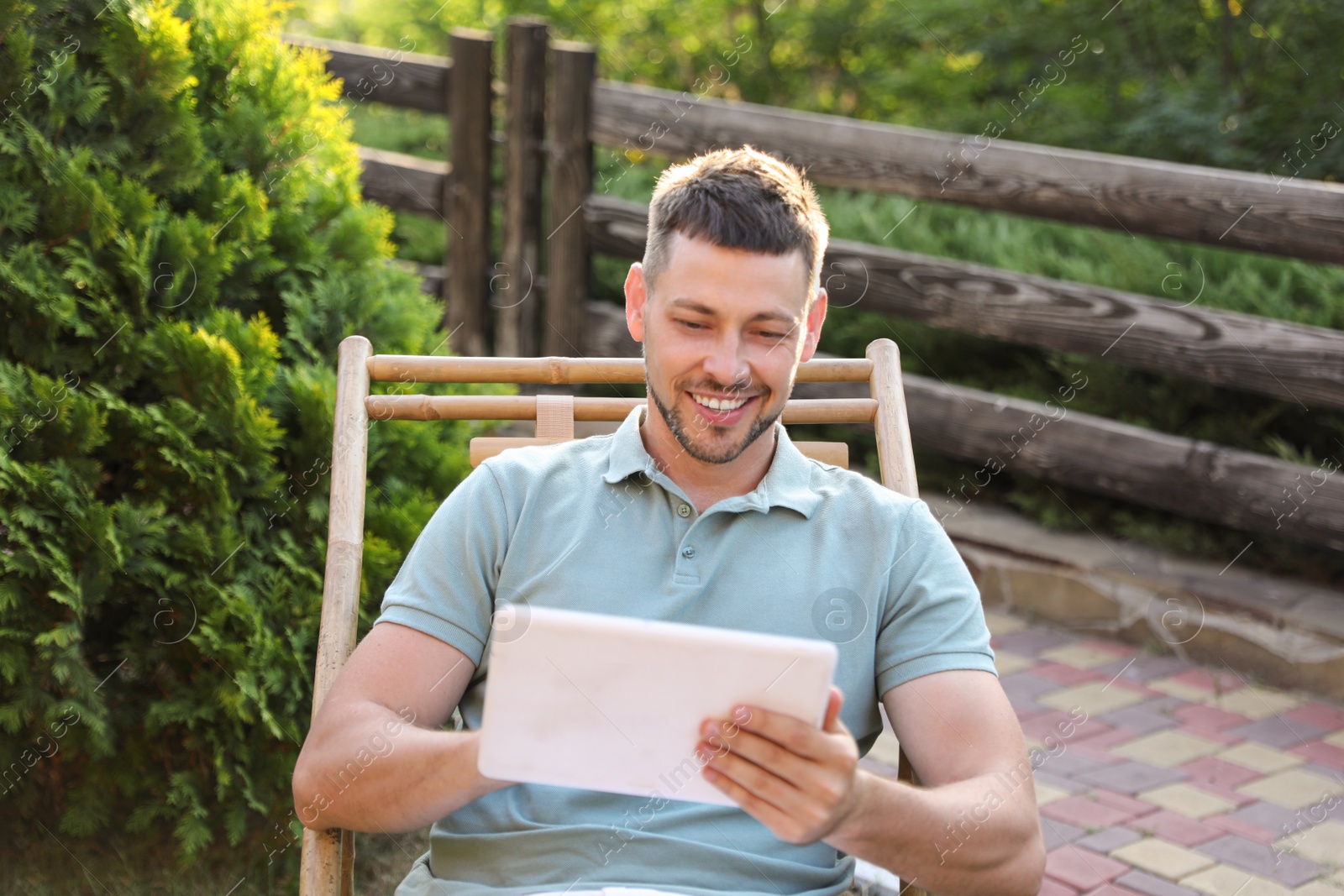 Image of Happy man using tablet in deck chair outdoors