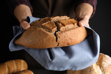 Photo of Man holding tasty bread on dark background, closeup