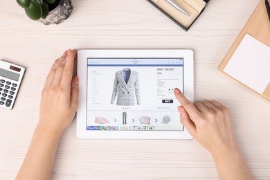 Photo of Woman with tablet shopping online at white wooden table, top view